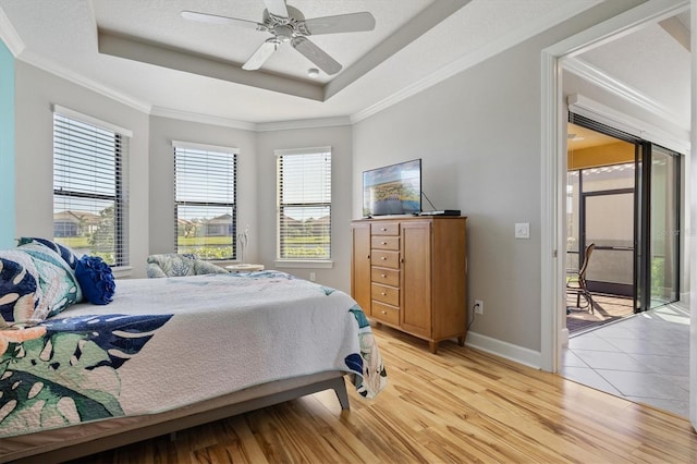 bedroom featuring access to exterior, ceiling fan, light hardwood / wood-style flooring, a tray ceiling, and ornamental molding