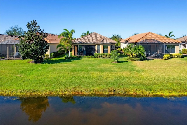 rear view of house with a lanai, a water view, and a lawn