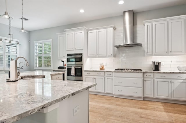 kitchen with stainless steel appliances, wall chimney exhaust hood, white cabinetry, and pendant lighting