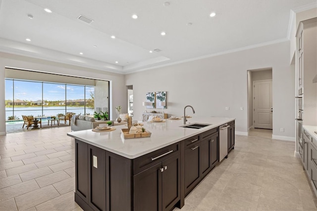 kitchen featuring appliances with stainless steel finishes, a raised ceiling, sink, a water view, and an island with sink