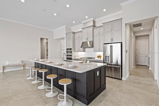 kitchen featuring appliances with stainless steel finishes, backsplash, a breakfast bar, gray cabinets, and an island with sink