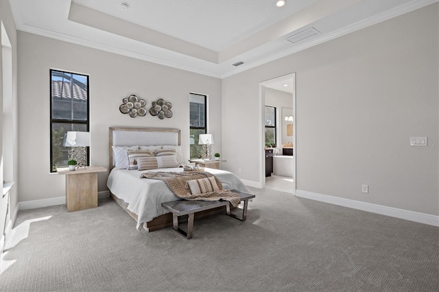 bedroom with a raised ceiling, light colored carpet, and ensuite bath