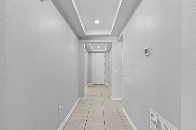 corridor featuring a tray ceiling and light tile patterned floors