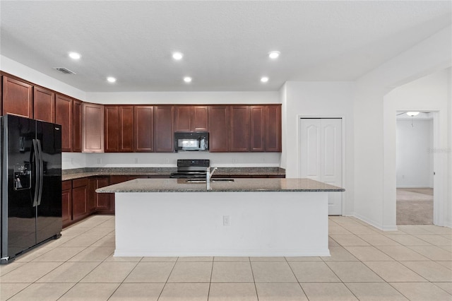 kitchen featuring a kitchen island with sink, black appliances, sink, dark stone countertops, and light tile patterned floors