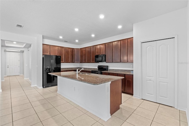 kitchen featuring dark stone counters, black appliances, sink, light tile patterned floors, and an island with sink