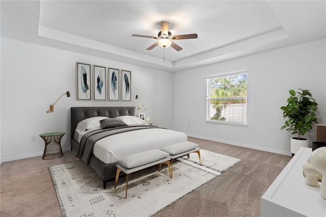 carpeted bedroom featuring a tray ceiling and ceiling fan