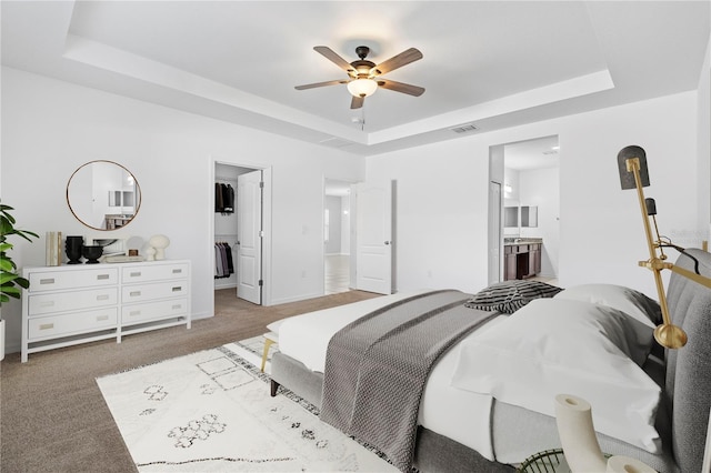 carpeted bedroom featuring ensuite bathroom, ceiling fan, and a tray ceiling