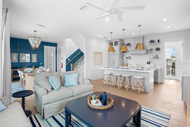 living room with ceiling fan with notable chandelier and light wood-type flooring