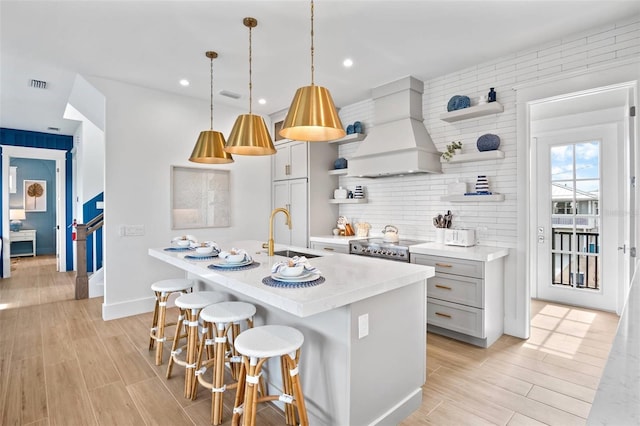 kitchen featuring custom exhaust hood, sink, hanging light fixtures, and light hardwood / wood-style flooring