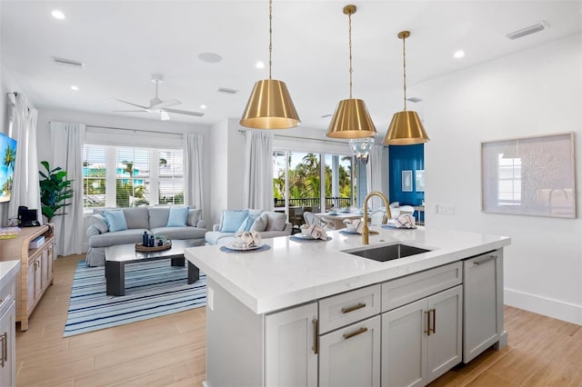 kitchen with light wood-type flooring, an island with sink, a healthy amount of sunlight, and sink