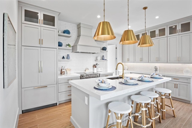 kitchen featuring custom range hood, an island with sink, light hardwood / wood-style flooring, and sink