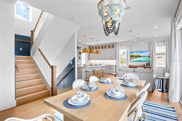 dining area with ceiling fan with notable chandelier, light hardwood / wood-style floors, and sink