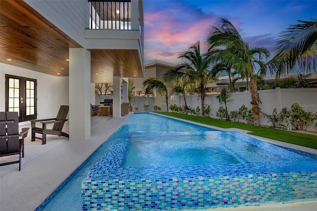 pool at dusk with a patio area, french doors, and exterior kitchen