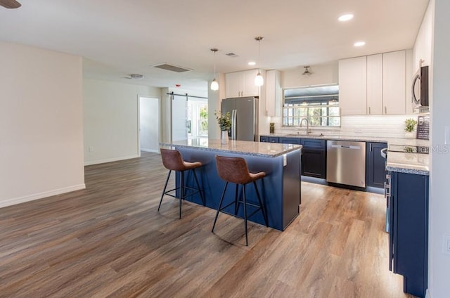 kitchen with light hardwood / wood-style floors, white cabinetry, appliances with stainless steel finishes, a center island, and a barn door