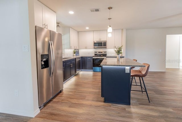 kitchen featuring dark stone counters, a kitchen bar, white cabinets, and appliances with stainless steel finishes