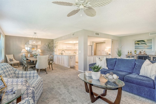 living room featuring ceiling fan with notable chandelier, light colored carpet, and a textured ceiling