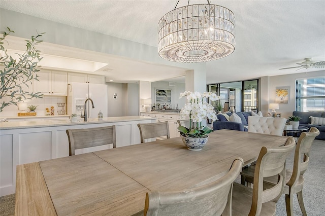 dining area featuring ceiling fan with notable chandelier, a textured ceiling, light colored carpet, and sink