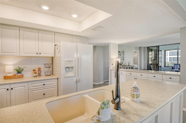 kitchen featuring tasteful backsplash, white fridge with ice dispenser, white cabinets, and a textured ceiling