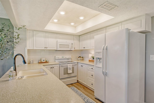 kitchen featuring white appliances, a tray ceiling, sink, white cabinets, and light hardwood / wood-style floors