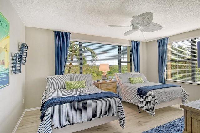 bedroom featuring a textured ceiling, light hardwood / wood-style floors, multiple windows, and ceiling fan