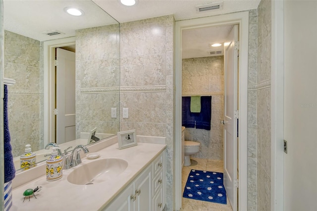 bathroom featuring tile patterned floors, vanity, toilet, and tile walls