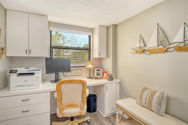 office area with a textured ceiling, built in desk, and light hardwood / wood-style flooring