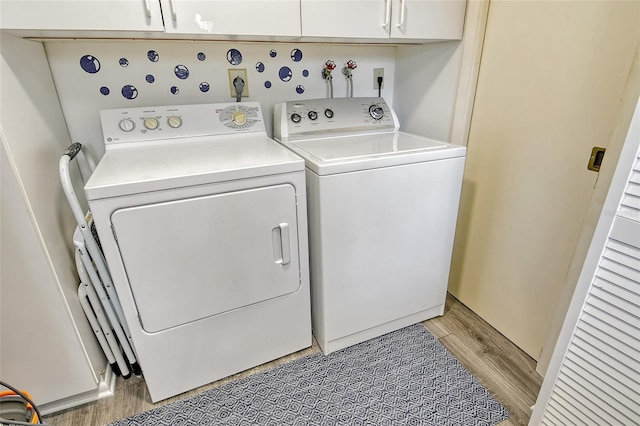 washroom featuring washing machine and dryer, cabinets, and light wood-type flooring