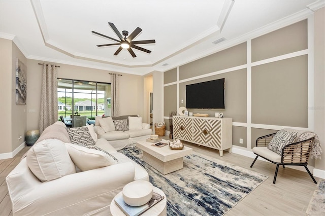 living room featuring crown molding, light wood-type flooring, ceiling fan, and a raised ceiling