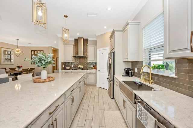 kitchen featuring pendant lighting, stainless steel appliances, wall chimney exhaust hood, and light stone counters