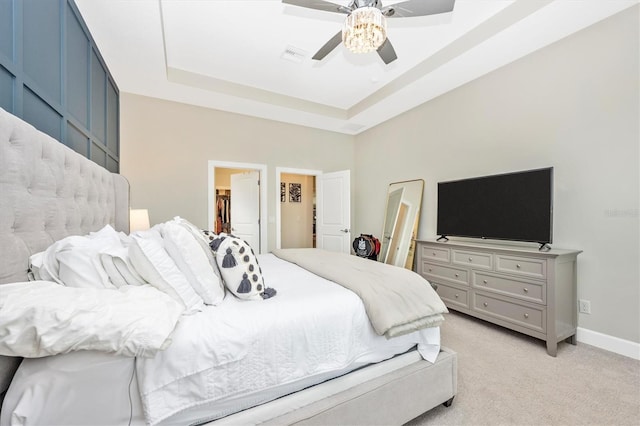 bedroom with light carpet, ceiling fan, a spacious closet, a tray ceiling, and a closet