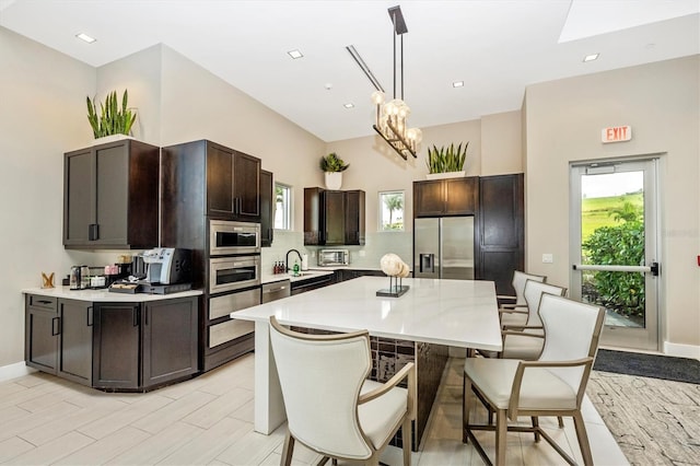 kitchen featuring stainless steel appliances, a kitchen island, decorative light fixtures, dark brown cabinetry, and sink