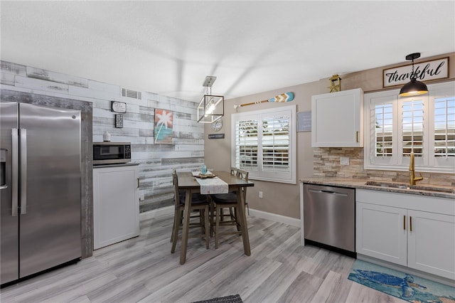 kitchen featuring stainless steel appliances, stone countertops, sink, decorative light fixtures, and white cabinets