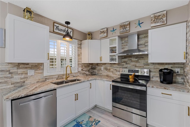 kitchen featuring white cabinetry, sink, appliances with stainless steel finishes, hanging light fixtures, and wall chimney range hood