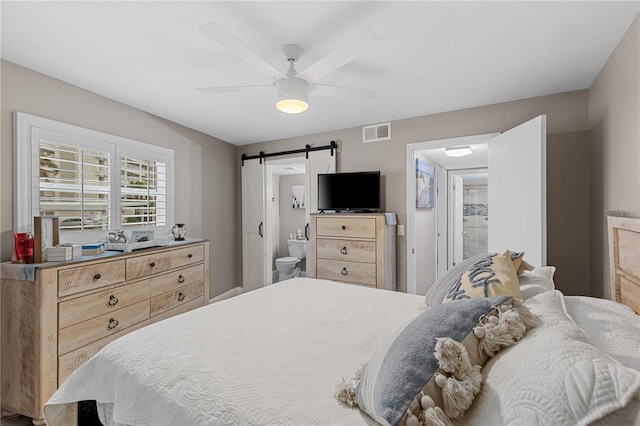 bedroom with a barn door, ceiling fan, and ensuite bath