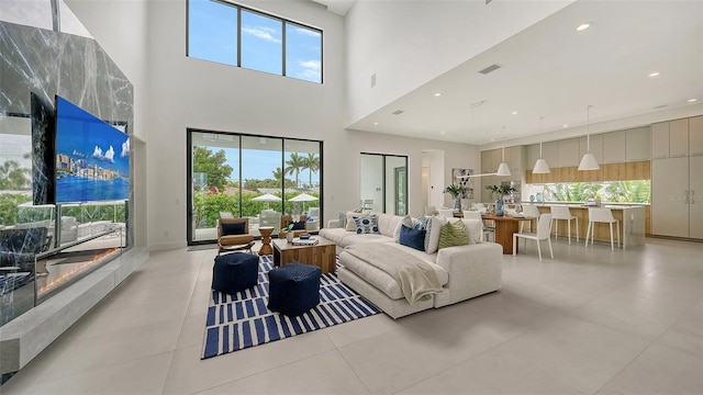 living room with a premium fireplace, light tile patterned floors, and a high ceiling