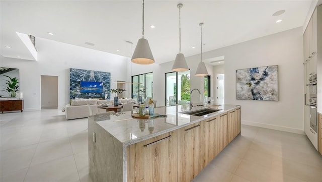 kitchen with pendant lighting, light brown cabinets, a large island with sink, sink, and light stone countertops