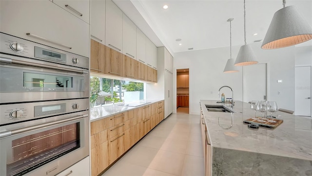 kitchen with light stone countertops, double oven, sink, pendant lighting, and white cabinets