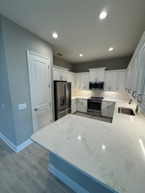 kitchen featuring stainless steel appliances, light stone counters, white cabinets, kitchen peninsula, and sink