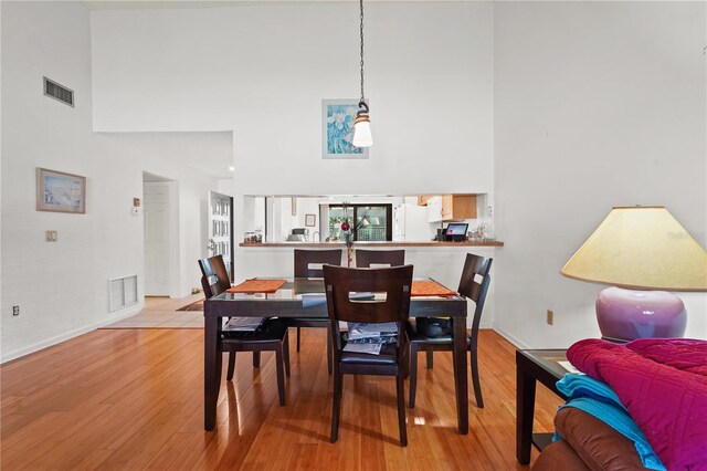 dining room with light wood-type flooring and a towering ceiling