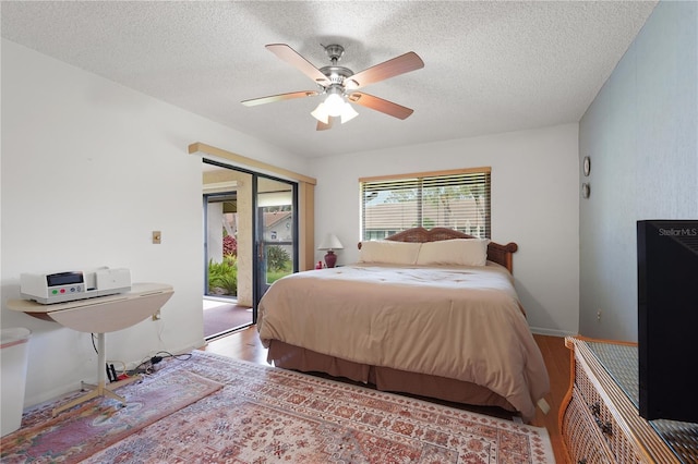 bedroom featuring access to exterior, a textured ceiling, a ceiling fan, and wood finished floors