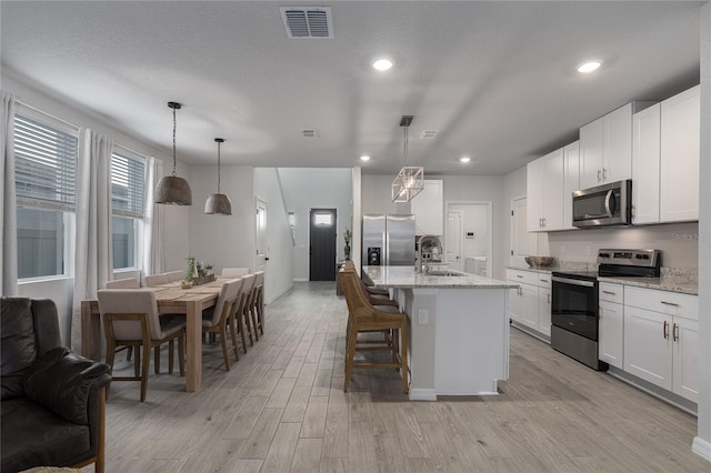 kitchen featuring white cabinetry, sink, appliances with stainless steel finishes, a kitchen island with sink, and pendant lighting