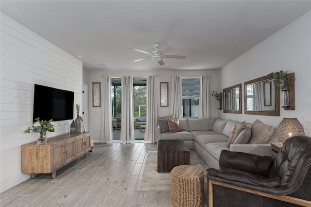 living room featuring light wood-type flooring, wooden walls, and ceiling fan