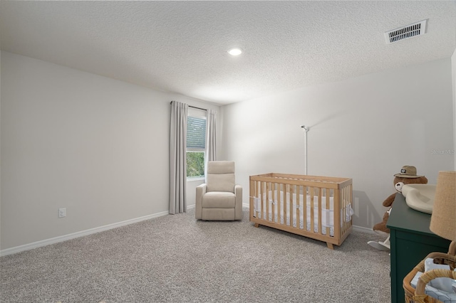 carpeted bedroom featuring a textured ceiling and a nursery area