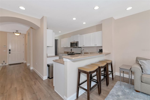 kitchen with a breakfast bar area, kitchen peninsula, white cabinetry, and light hardwood / wood-style flooring