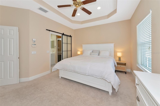 carpeted bedroom with a barn door, a tray ceiling, and ceiling fan