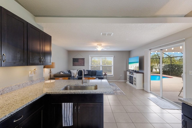 kitchen featuring kitchen peninsula, sink, a textured ceiling, light tile patterned floors, and light stone counters