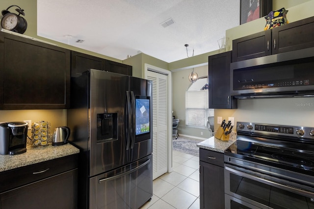 kitchen with a textured ceiling, light tile patterned floors, stainless steel appliances, and light stone countertops