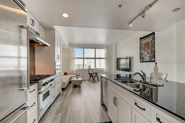 kitchen with dark stone counters, high end appliances, sink, white cabinetry, and light wood-type flooring