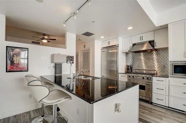 kitchen with built in appliances, white cabinetry, sink, dark stone countertops, and light hardwood / wood-style flooring