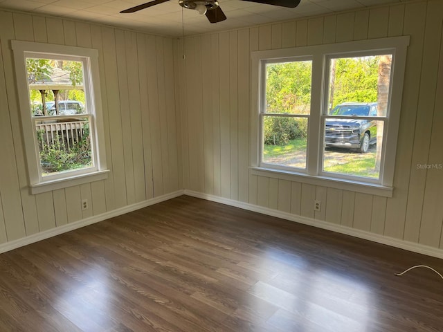 empty room featuring dark hardwood / wood-style flooring, ceiling fan, and wooden walls